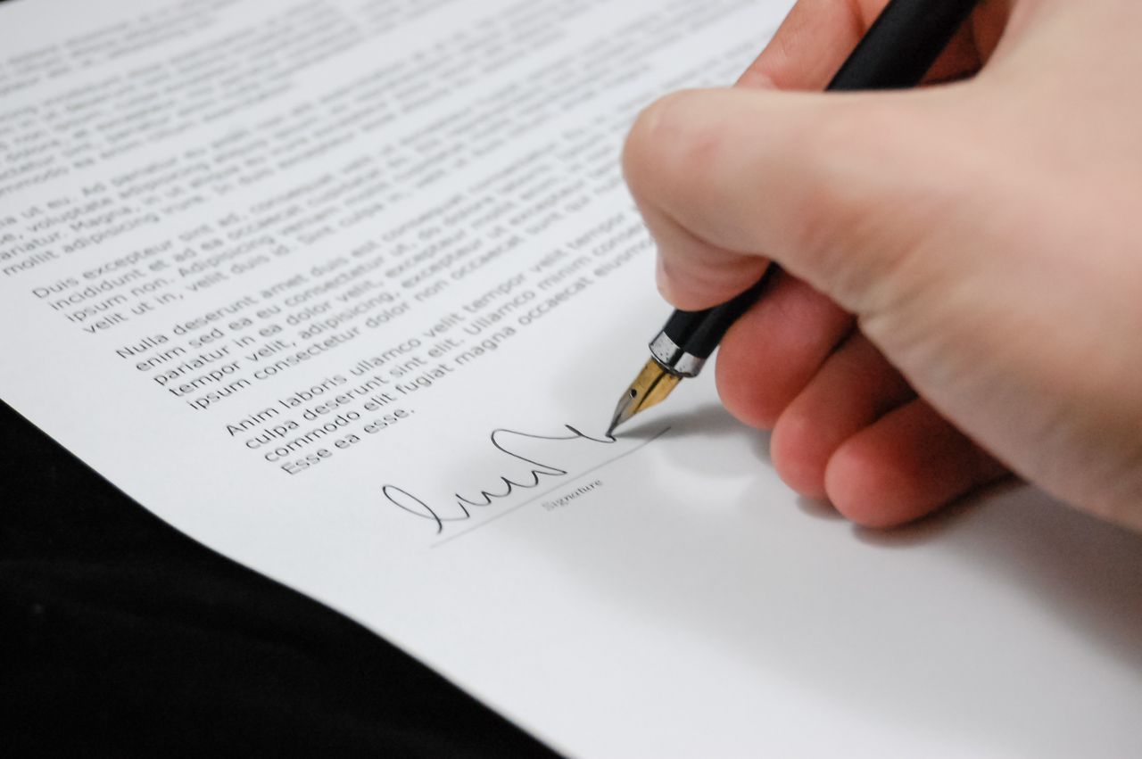 gallery-03 Close-up of a hand signing a legal document with a fountain pen, symbolizing signature and agreement.