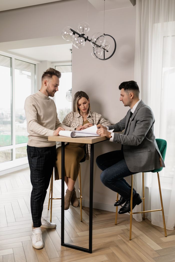featured-images-01 Pregnant couple reviewing property documents with a real estate agent in a bright modern interior.