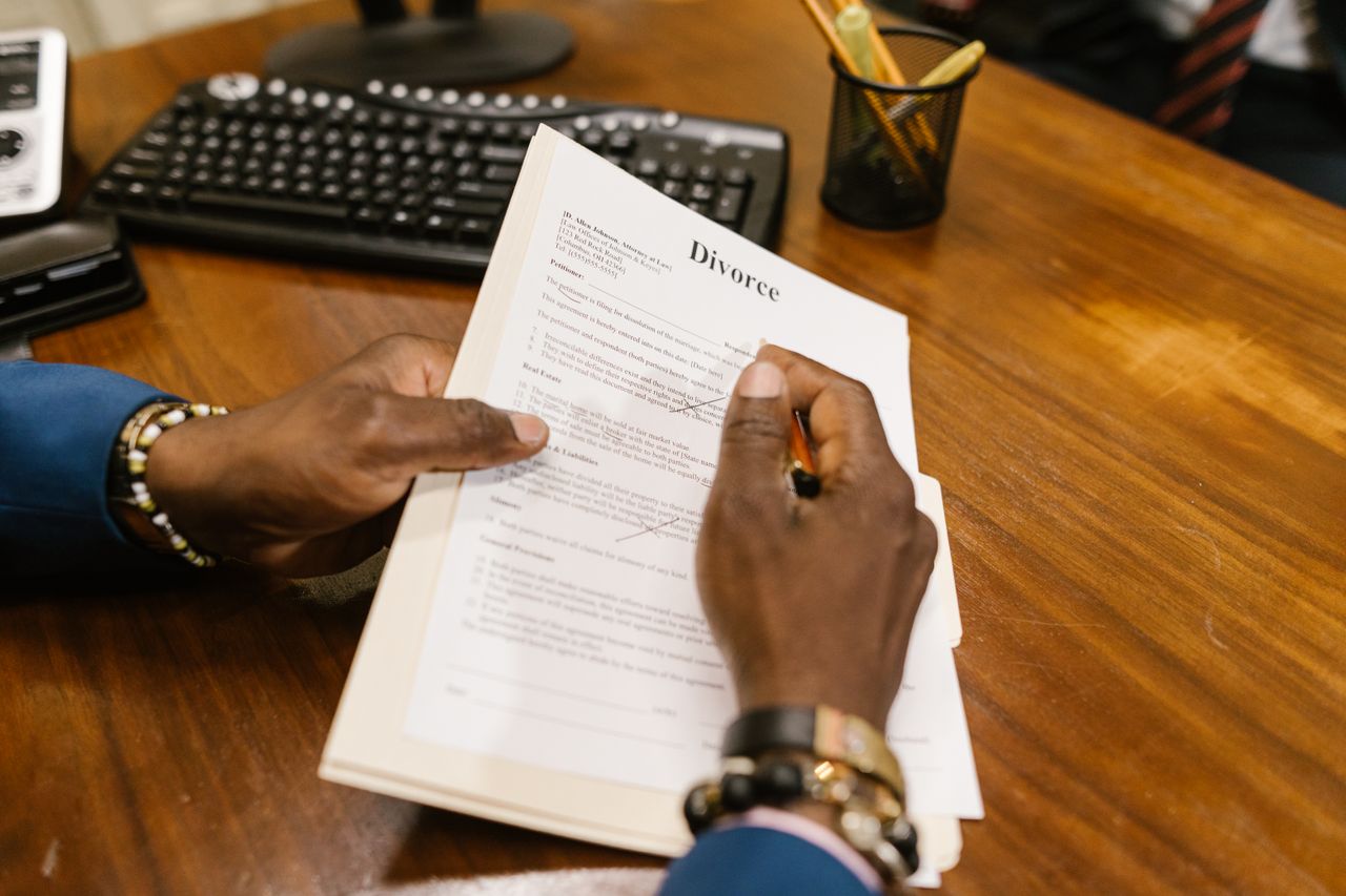 about-me-01 A person signs official divorce documents at an office desk.