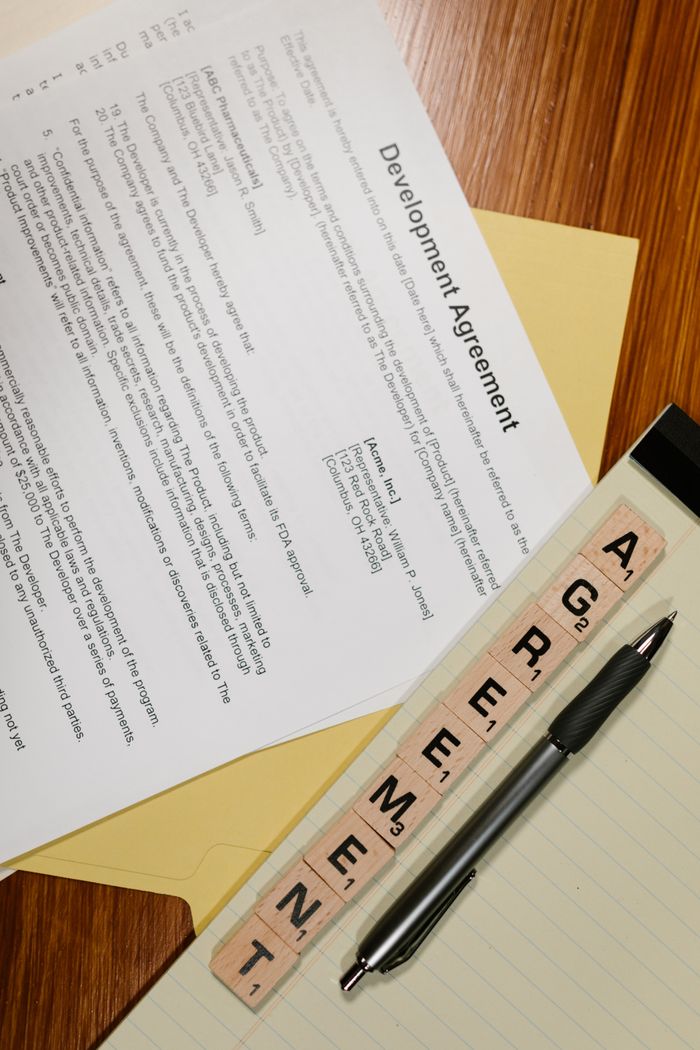 gallery-09 A vertical shot showcasing agreement documents, Scrabble tiles, and a pen on a desk.