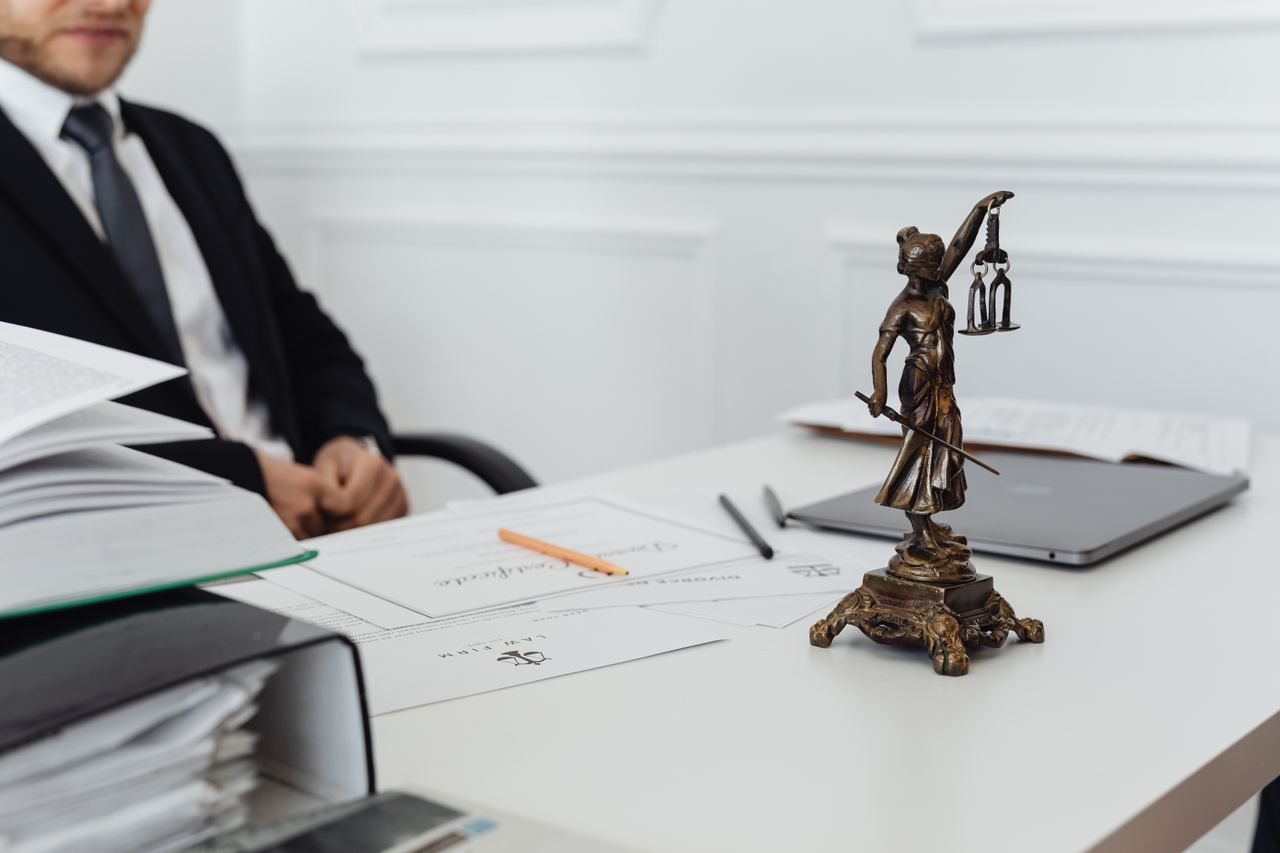featured-images-05 A legal professional's workspace featuring Lady Justice statue, documents, and a laptop.
