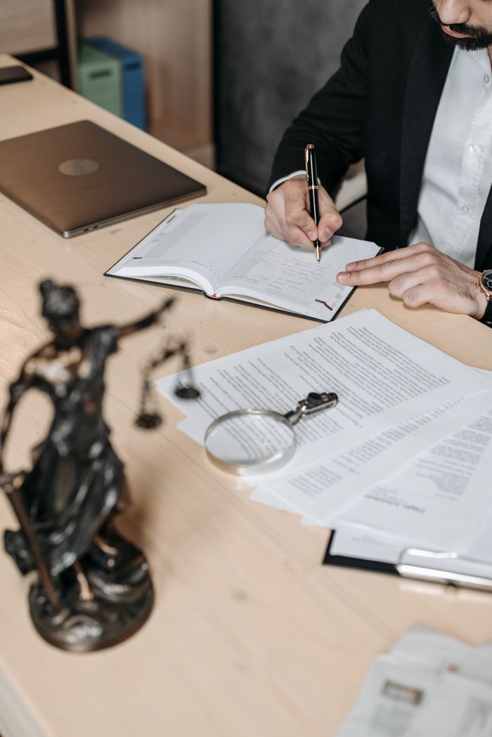 gallery-02 Professional working on documents at desk with legal statue and magnifying glass.