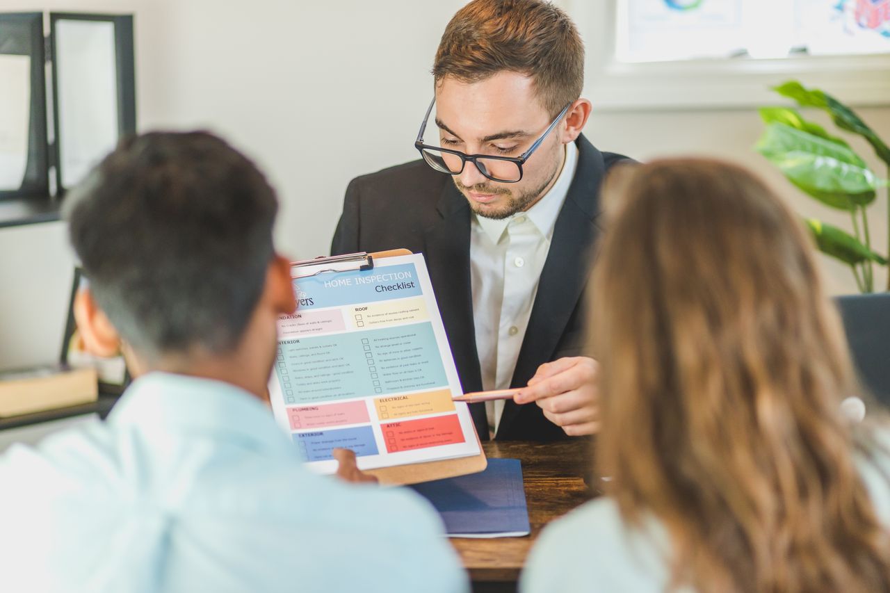 featured-images-02 Real estate agent explaining home inspection checklist to clients in an office setting.
