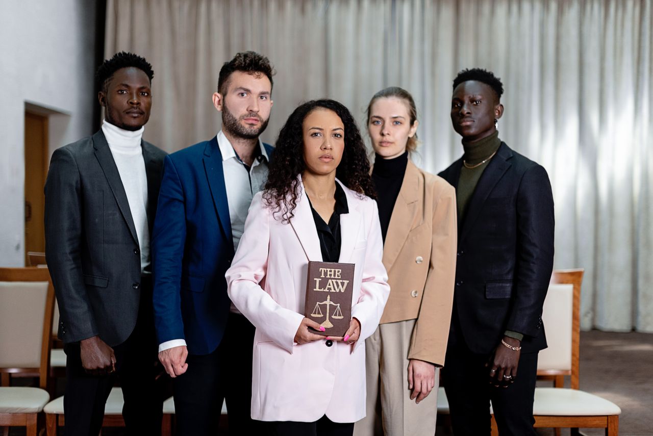 services-02 A diverse group of five lawyers posing confidently with a law book in an office setting.
