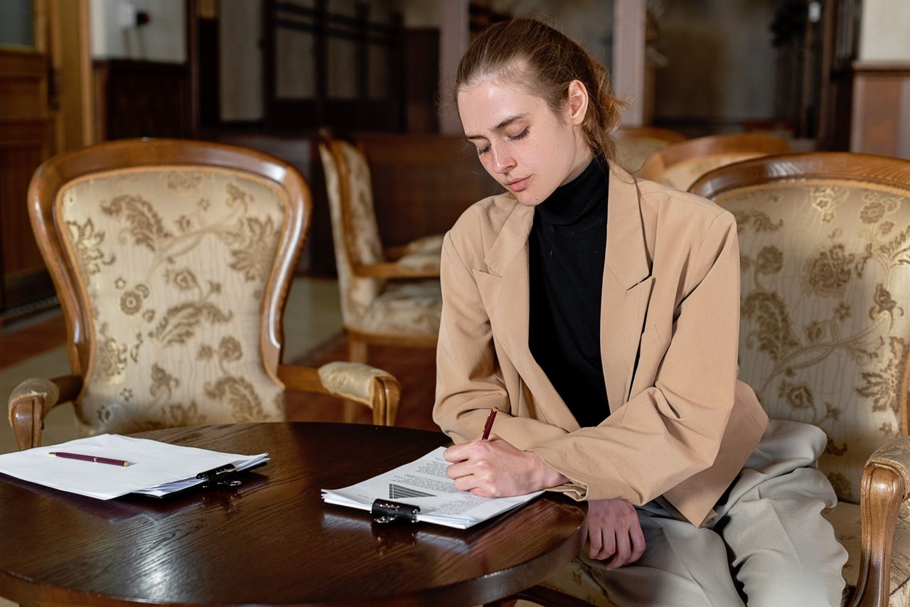 engagement-photography-03 Young woman in a brown blazer signing documents at a table in a stylish office.