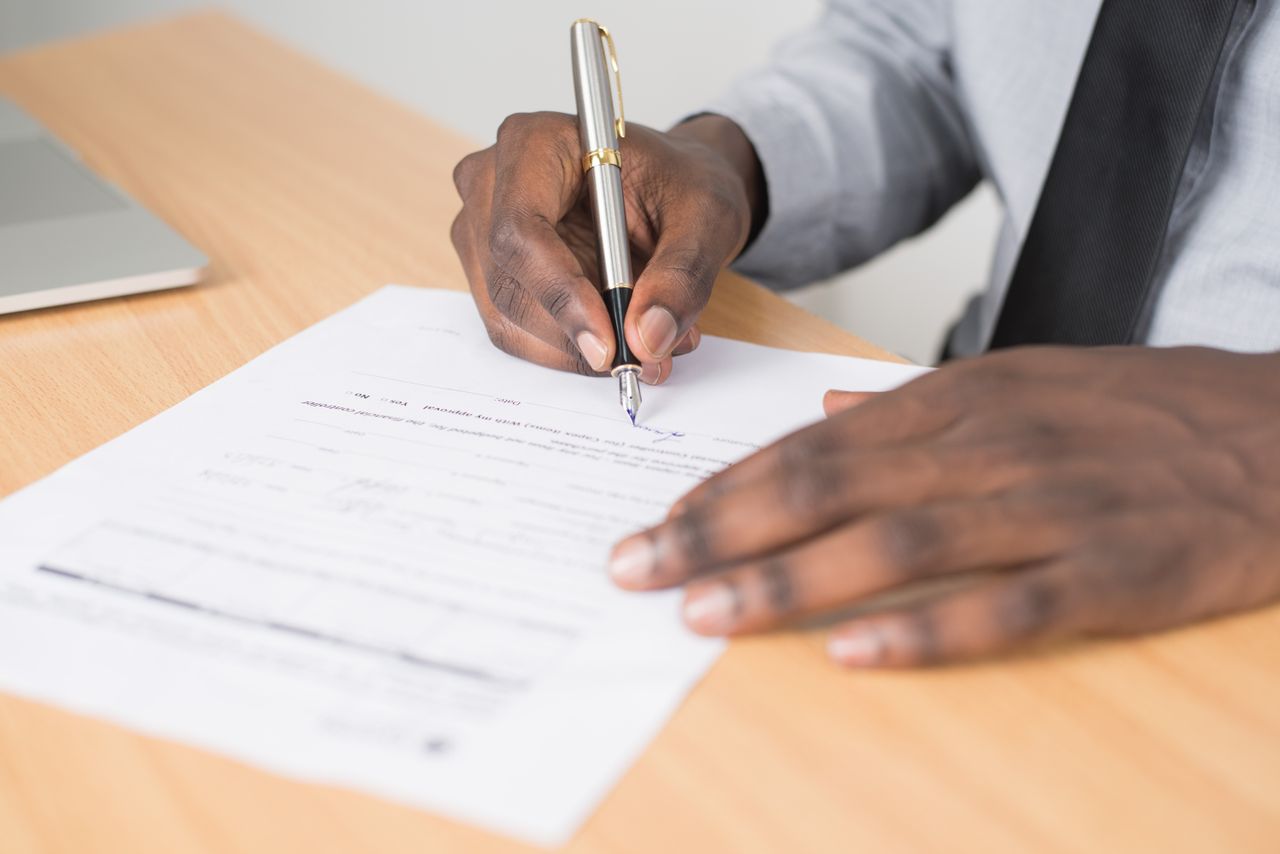 gallery-04 Close-up of a businessman signing a contract at an office desk.